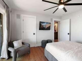 This inviting bedroom features a comfortable bed, a cozy armchair with a plush throw pillow, and a wall-mounted TV displaying a scenic bridge.