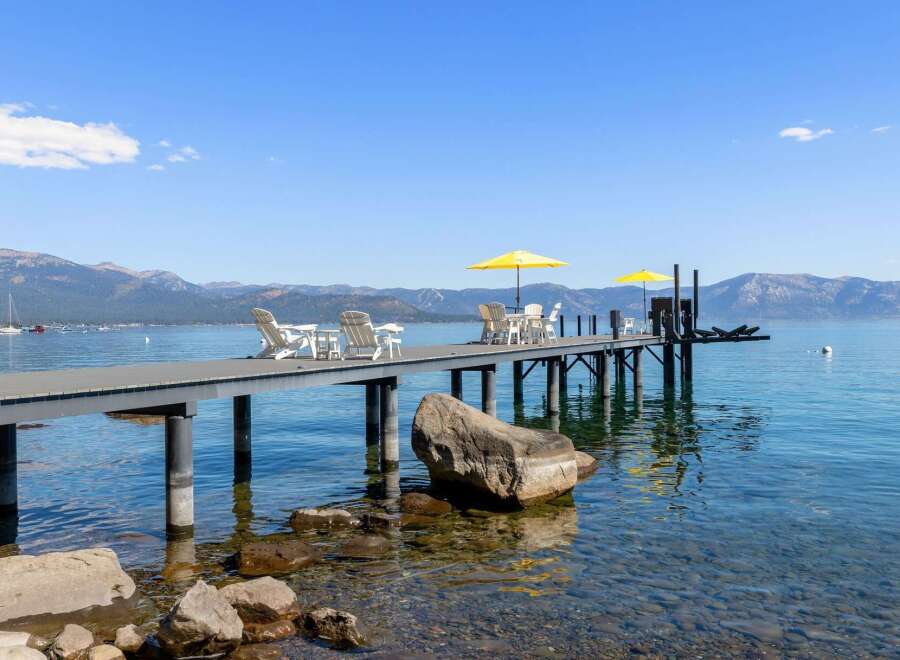 Enjoy breathtaking lake views from this stunning property featuring a private dock with ample seating and yellow umbrellas for shade.