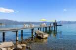 Enjoy breathtaking lake views from this stunning property featuring a private dock with ample seating and yellow umbrellas for shade.