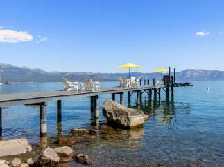Enjoy breathtaking lake views from this stunning property featuring a private dock with ample seating and yellow umbrellas for shade.