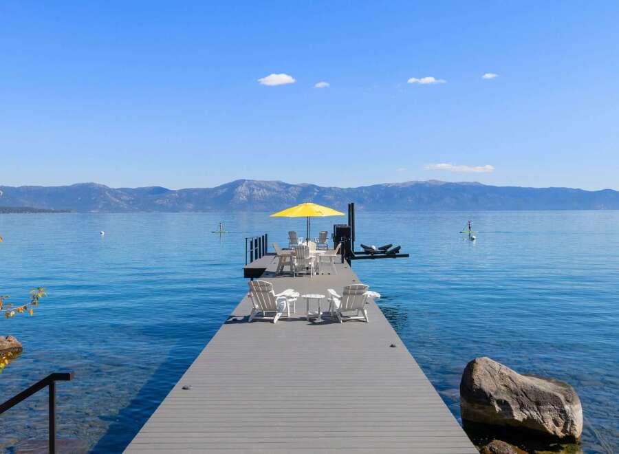 Enjoy breathtaking lake views from this stunning property featuring a private dock with ample seating and a vibrant yellow umbrella.