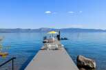 Enjoy breathtaking lake views from this stunning property featuring a private dock with ample seating and a vibrant yellow umbrella.