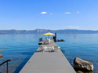 Enjoy breathtaking lake views from this stunning property featuring a private dock with ample seating and a vibrant yellow umbrella.