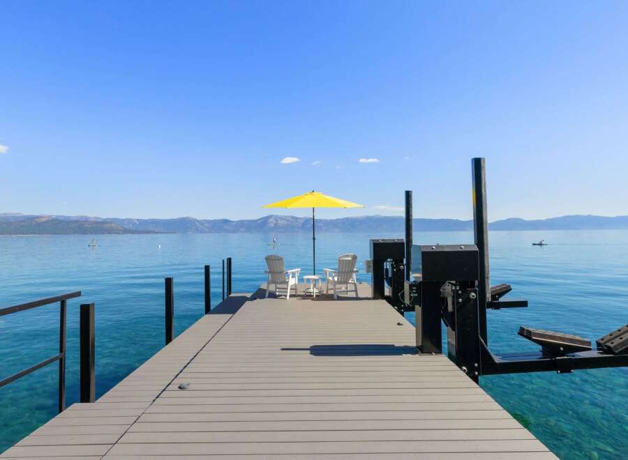 Enjoy breathtaking lake views from this stunning property featuring a private dock with seating and a vibrant yellow umbrella.