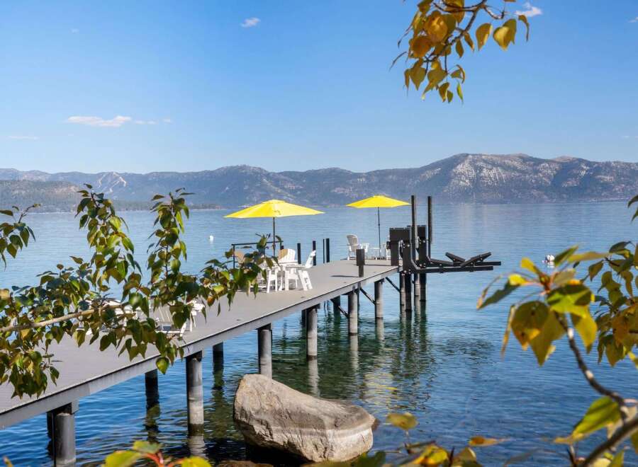 Enjoy breathtaking lake views from this stunning property featuring a private dock with ample seating and two vibrant yellow umbrellas for shade.