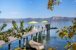 Enjoy breathtaking lake views from this stunning property featuring a private dock with ample seating and two vibrant yellow umbrellas for shade.