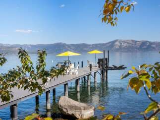 Enjoy breathtaking lake views from this stunning property featuring a private dock with ample seating and two vibrant yellow umbrellas for shade.