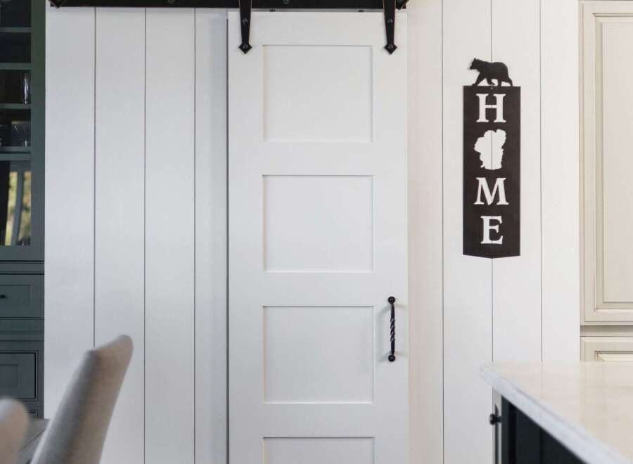 This charming farmhouse-style kitchen features a striking white paneled wall adorned with a large round clock and a decorative 'HOME' sign.