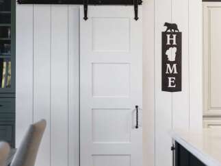 This charming farmhouse-style kitchen features a striking white paneled wall adorned with a large round clock and a decorative 'HOME' sign.