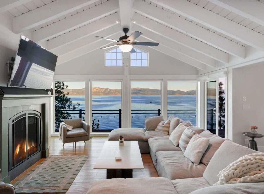 Experience breathtaking lake views from this stunning living room, featuring a vaulted ceiling with exposed beams and a cozy fireplace.