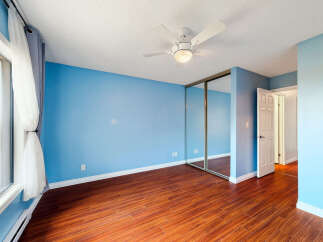 Step into this bright and airy bedroom featuring a soothing light blue accent wall and rich hardwood flooring.