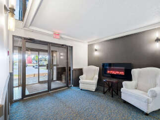 Step into a welcoming lobby featuring a cozy seating area with two plush armchairs and a modern electric fireplace.