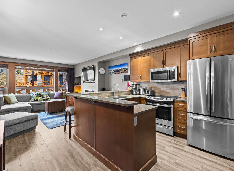 This open-concept living space features a modern kitchen with stainless steel appliances, granite countertops, and ample wooden cabinetry.