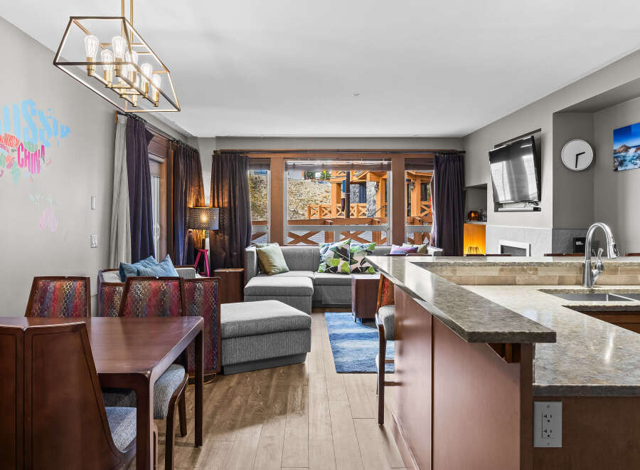 This open-concept living space features a modern dining area with a rich wood table and upholstered chairs, flowing seamlessly into a comfortable living room with a sectional sofa and vibrant accent pillows.