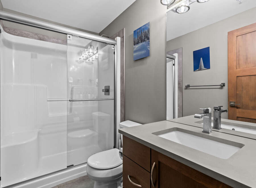 This modern bathroom features a sleek white shower stall with glass doors, complemented by a minimalist toilet and a floating vanity with a concrete countertop.
