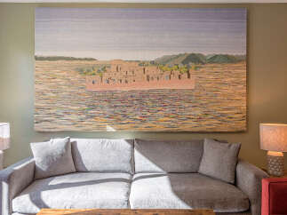 Experience tranquility in this beautifully appointed living space, featuring a large, textured tapestry depicting a desert village scene above a plush grey sofa.