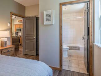 This charming property offers a comfortable bedroom with a bedside lamp and a wooden nightstand, leading to a well-equipped kitchen area.