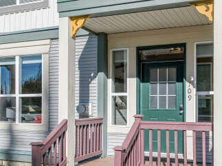 Welcome to this charming home featuring a welcoming covered porch with a vibrant green door and decorative accents.