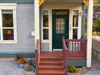 Welcome to this charming home featuring a classic dark green front door with a multi-pane window, complemented by a welcoming porch and steps.