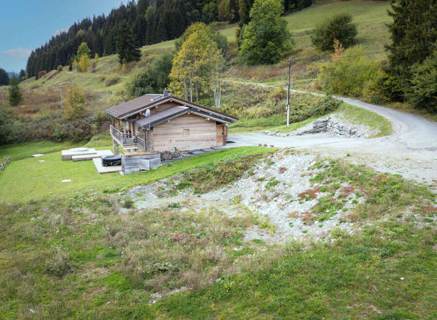 Nestled amidst rolling green hills and a dense forest, this charming wooden cabin offers a serene mountain retreat.
