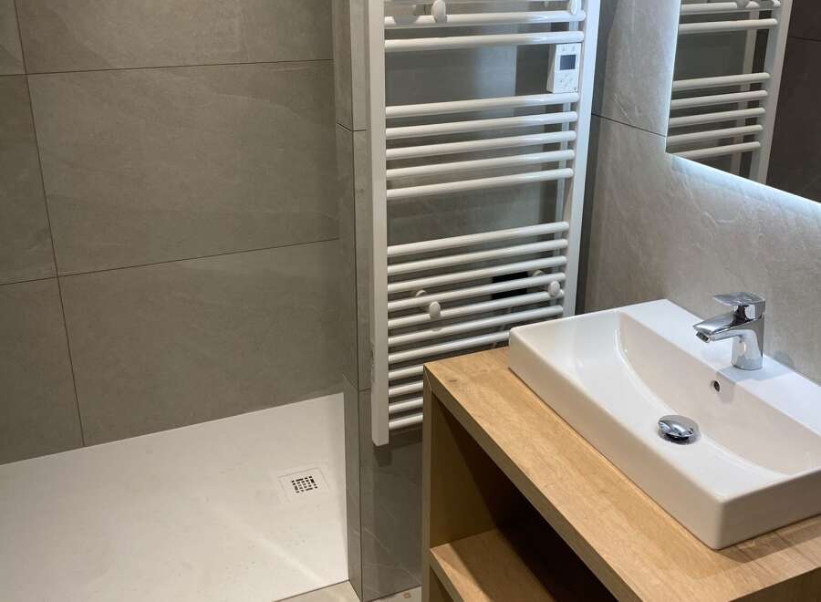 This modern bathroom features a sleek white sink atop a warm wooden vanity, complemented by a chrome faucet.