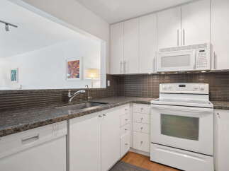 This kitchen boasts sleek white cabinetry and a modern granite countertop, complemented by a stylish tiled backsplash.