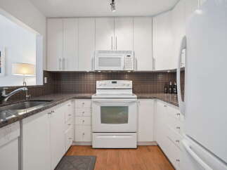 This U-shaped kitchen boasts modern white cabinetry and sleek granite countertops, offering ample storage and workspace.