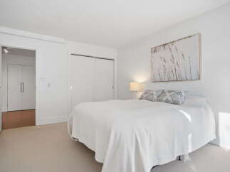 This bright and airy bedroom features a comfortable queen-size bed adorned with decorative pillows and a crisp white duvet.