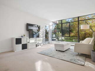 Experience abundant natural light in this living room, featuring a large wall of windows overlooking a lush, green backyard.