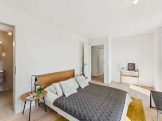 Experience modern comfort in this beautifully appointed bedroom, featuring a plush queen-sized bed with a stylish wooden headboard and a cozy quilted duvet.