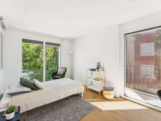 Experience serene living in this bright bedroom, featuring a comfortable bed adorned with plush pillows and a textured throw.