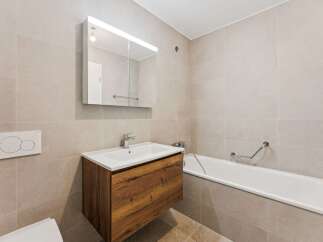 This modern bathroom features a floating wooden vanity with a white basin and a sleek chrome faucet, complemented by a large mirrored medicine cabinet with integrated lighting.