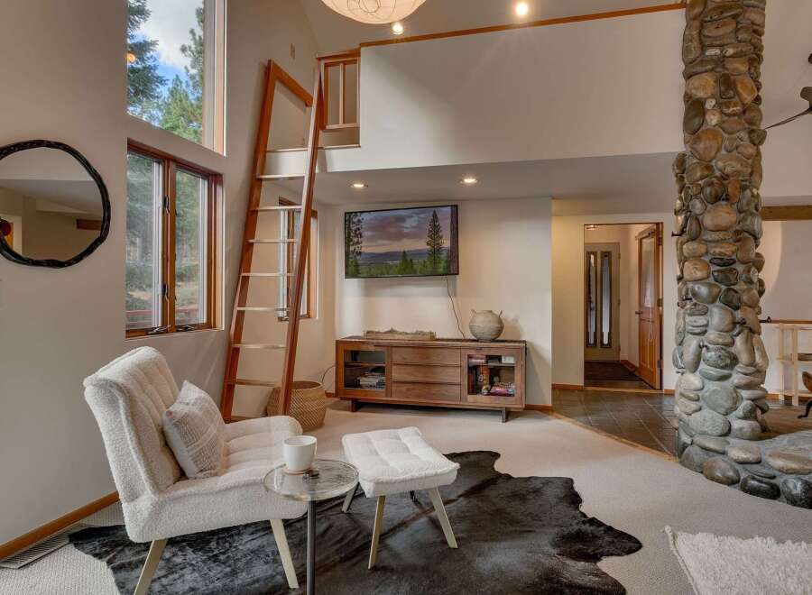 Experience rustic charm in this inviting living space, featuring a towering stone fireplace and a unique wooden ladder leading to a loft.