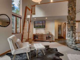 Experience rustic charm in this inviting living space, featuring a towering stone fireplace and a unique wooden ladder leading to a loft.