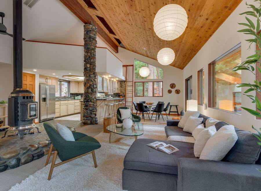 Experience the warmth and natural beauty of this stunning living space, featuring a striking stone-clad fireplace and a vaulted wood-beamed ceiling that creates an airy, open atmosphere.