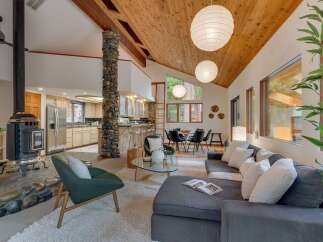 Experience the warmth and natural beauty of this stunning living space, featuring a striking stone-clad fireplace and a vaulted wood-beamed ceiling that creates an airy, open atmosphere.