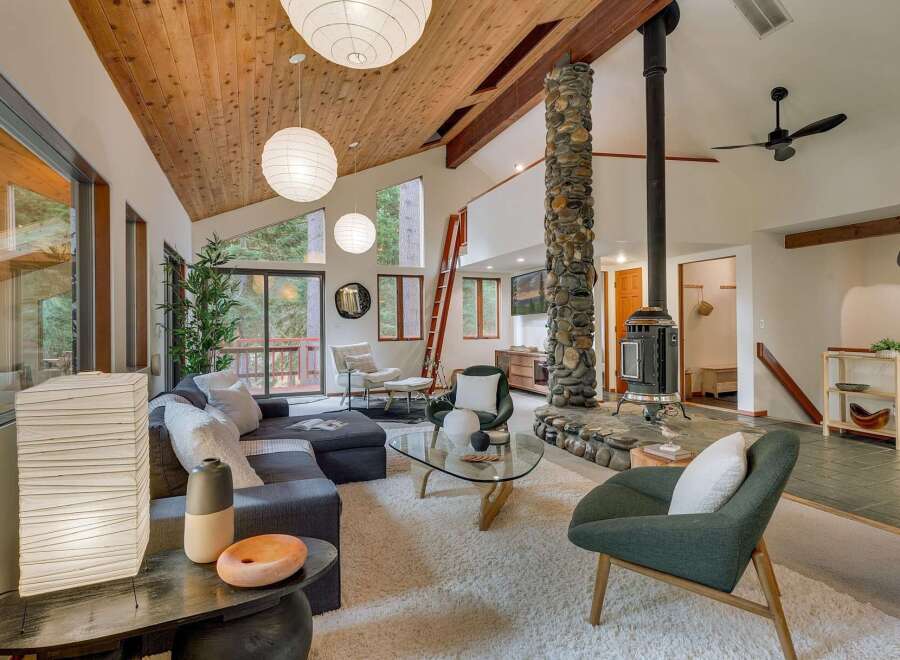 Experience the warmth and rustic charm of this spacious living area, featuring a striking floor-to-ceiling stone fireplace and a vaulted wood-paneled ceiling.
