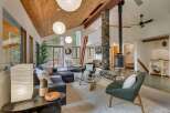 Experience the warmth and rustic charm of this spacious living area, featuring a striking floor-to-ceiling stone fireplace and a vaulted wood-paneled ceiling.
