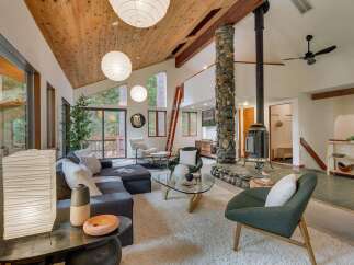 Experience the warmth and rustic charm of this spacious living area, featuring a striking floor-to-ceiling stone fireplace and a vaulted wood-paneled ceiling.