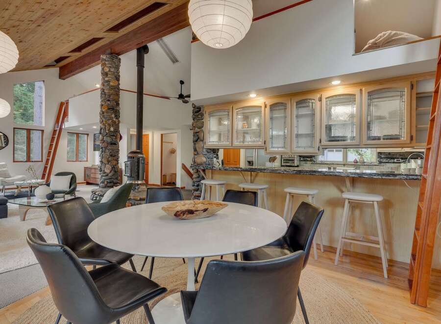 Experience open-concept living with a stunning vaulted wood-beamed ceiling and a striking stone-clad pillar supporting a wood-burning stove.