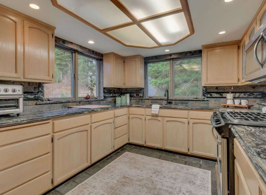 This spacious kitchen boasts light wood cabinetry complemented by dark granite countertops and a decorative tile backsplash.
