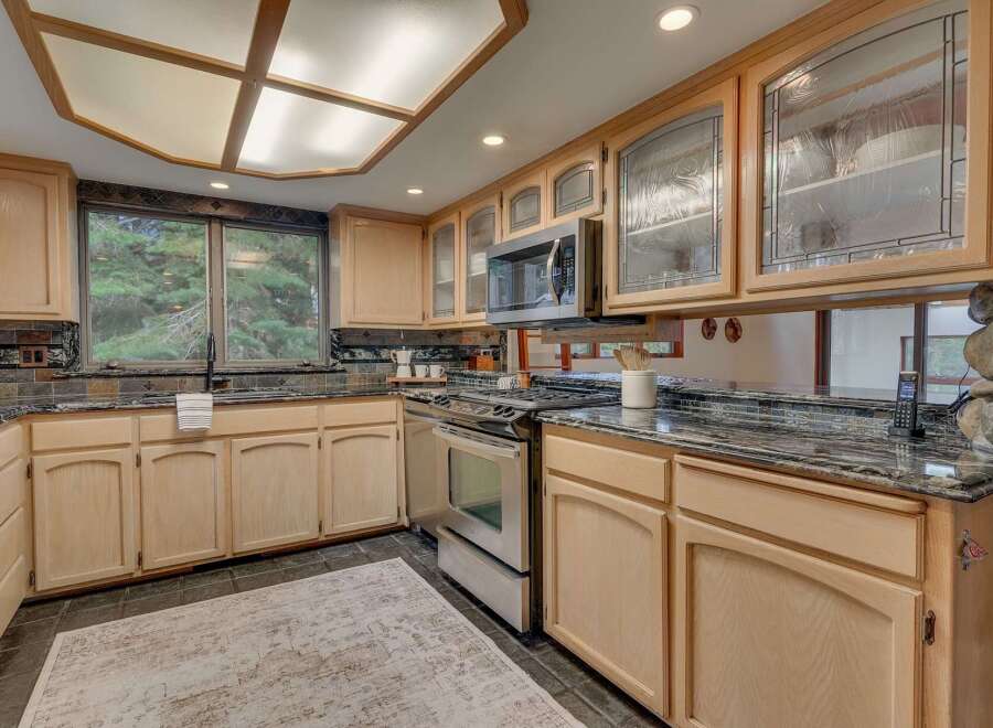 This kitchen boasts light wood cabinetry with decorative glass-front upper cabinets, complemented by a sleek stainless steel range and microwave.