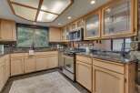 This kitchen boasts light wood cabinetry with decorative glass-front upper cabinets, complemented by a sleek stainless steel range and microwave.
