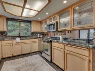 This kitchen boasts light wood cabinetry with decorative glass-front upper cabinets, complemented by a sleek stainless steel range and microwave.