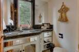 This charming bathroom features a granite countertop with an undermount sink and dark bronze fixtures, complemented by a large mirror reflecting the serene forest view outside the window.