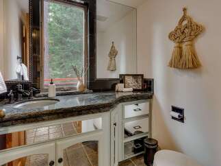 This charming bathroom features a granite countertop with an undermount sink and dark bronze fixtures, complemented by a large mirror reflecting the serene forest view outside the window.