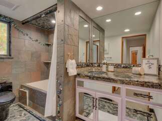 This unique bathroom features a striking slate tile shower and tub surround, complemented by a decorative mosaic tile accent that flows across the walls and ceiling.