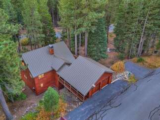Nestled amidst towering pine trees, this charming red wood-sided home offers a serene retreat.