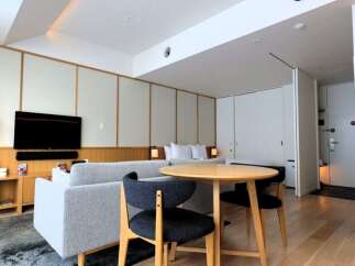 Experience modern living in this stylish studio apartment, featuring a comfortable sofa, a sleek flat-screen TV, and a cozy dining area with a round wooden table and chairs.