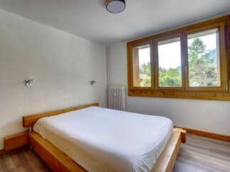 Experience comfort and style in this inviting bedroom, featuring a sturdy wooden bed frame and a large window offering picturesque views of the surrounding nature.